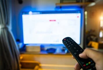 A person holding a remote control, watching news to analyze the trading charts